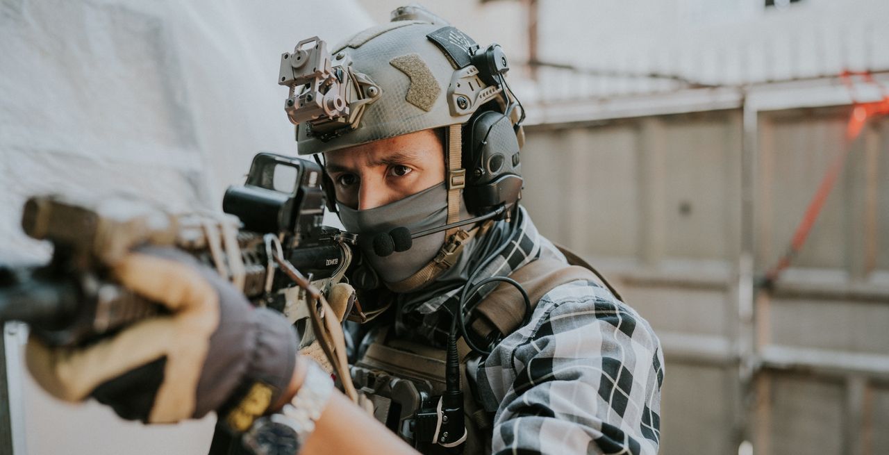 Close-up of a soldier with tactical gear aiming his weapon in an outdoor setting.