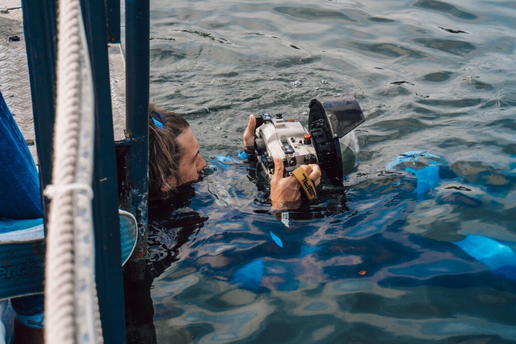 Photographer holding camera in water, capturing ocean scenes.
